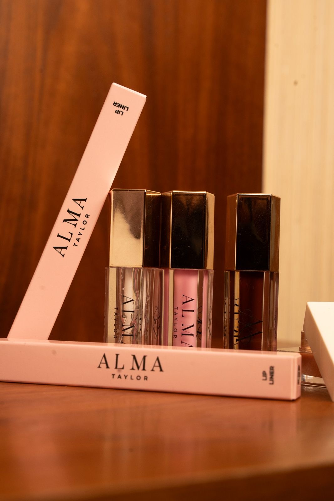 ALMA lip glosses and lip liner packaging styled on a wooden vanity