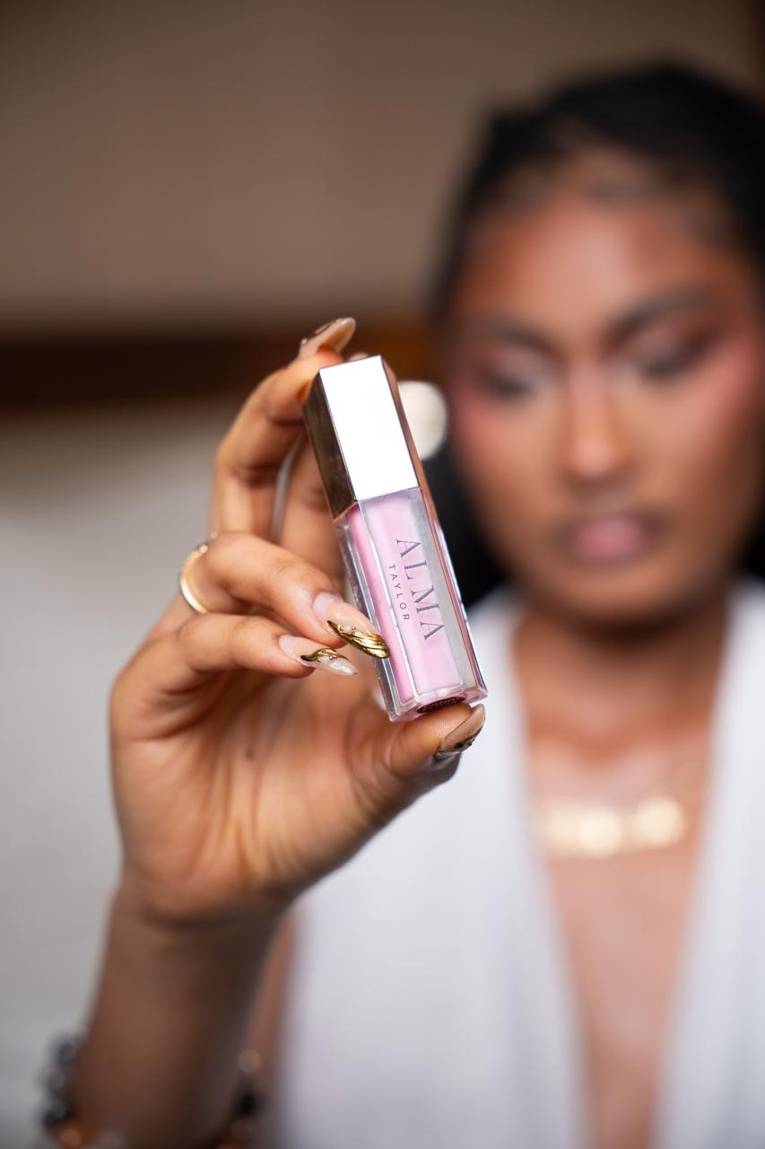 ALMA Taylor lip gloss tube in a soft pink shade held up to the light